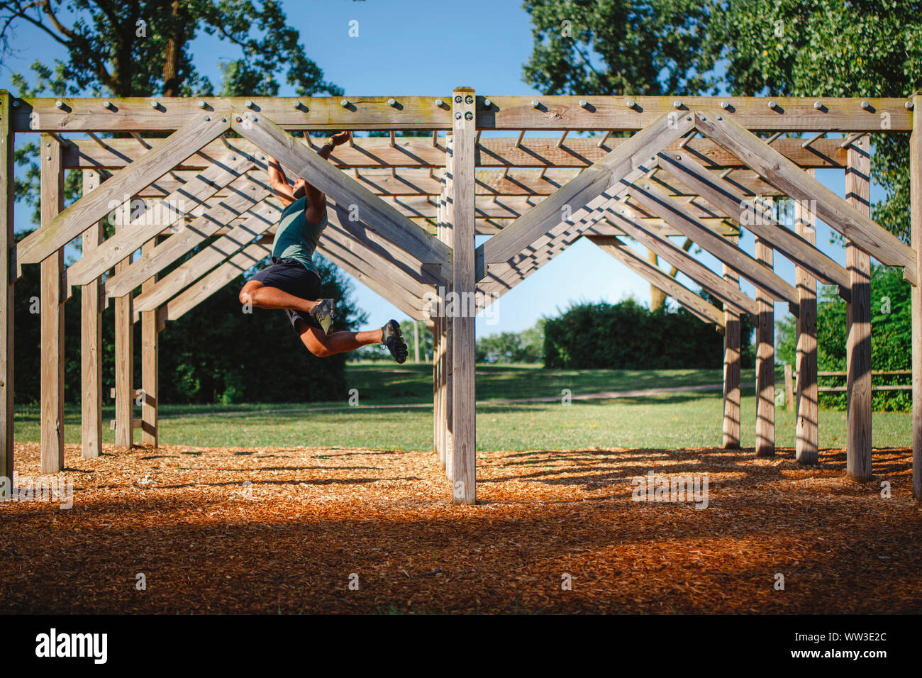 Side View of an athletic male swinging across monkey bars in a park