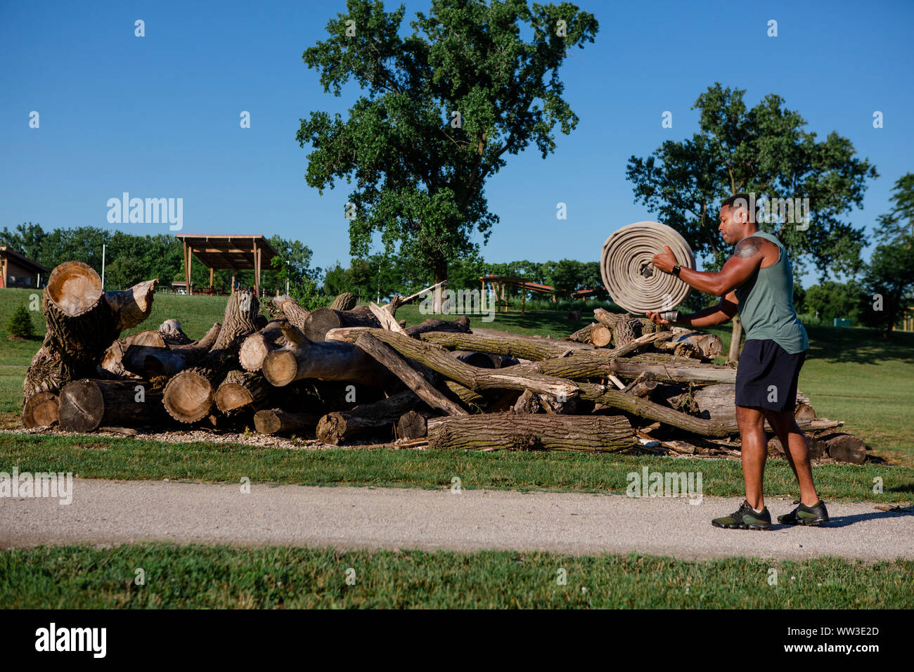 An athletic man prepares to throw a roll of heavy firehose in a park Stock Photo