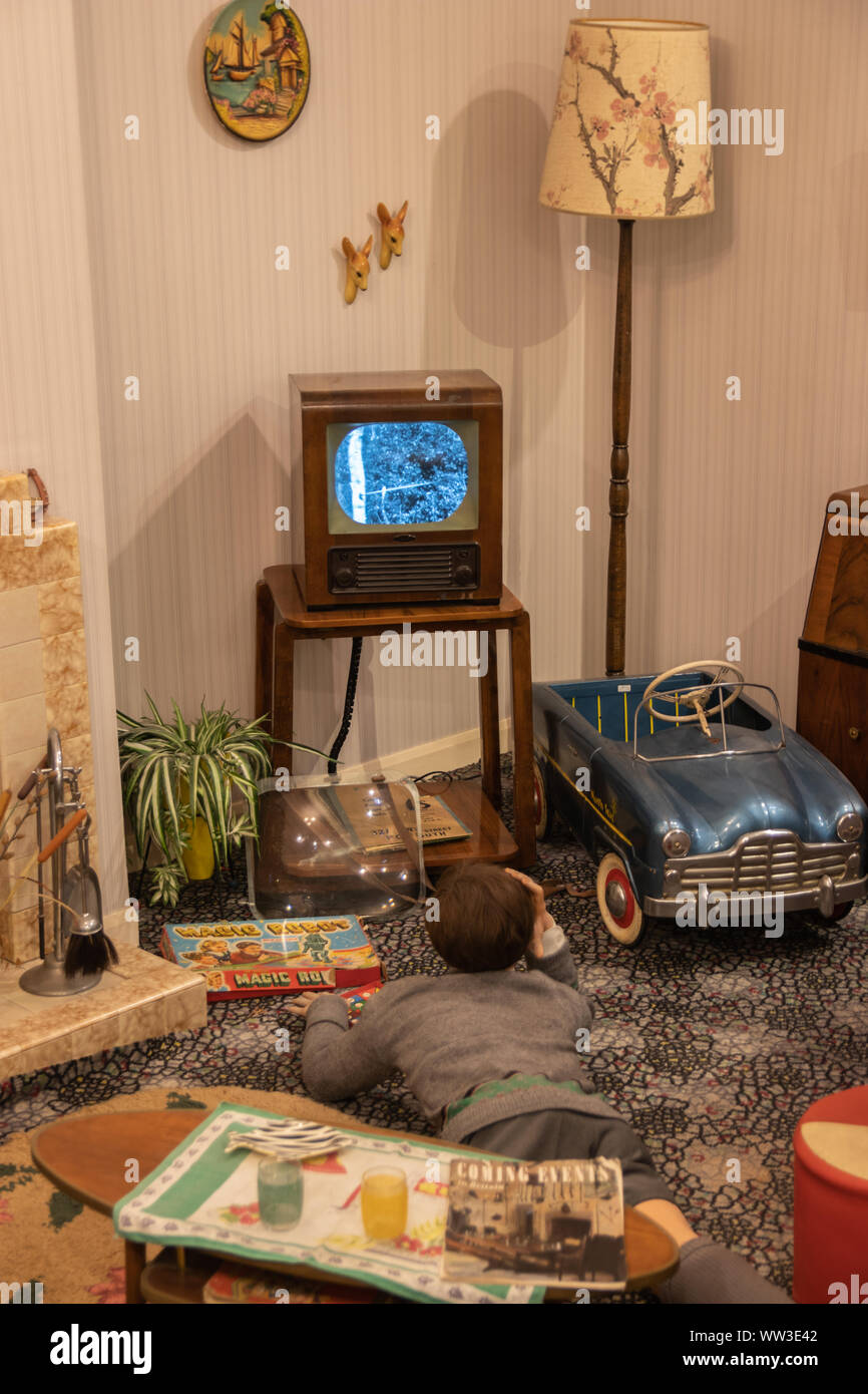 A scene from a 1960's living room or lounge with a boy laying on the floor watching a vintage black and white TV Stock Photo