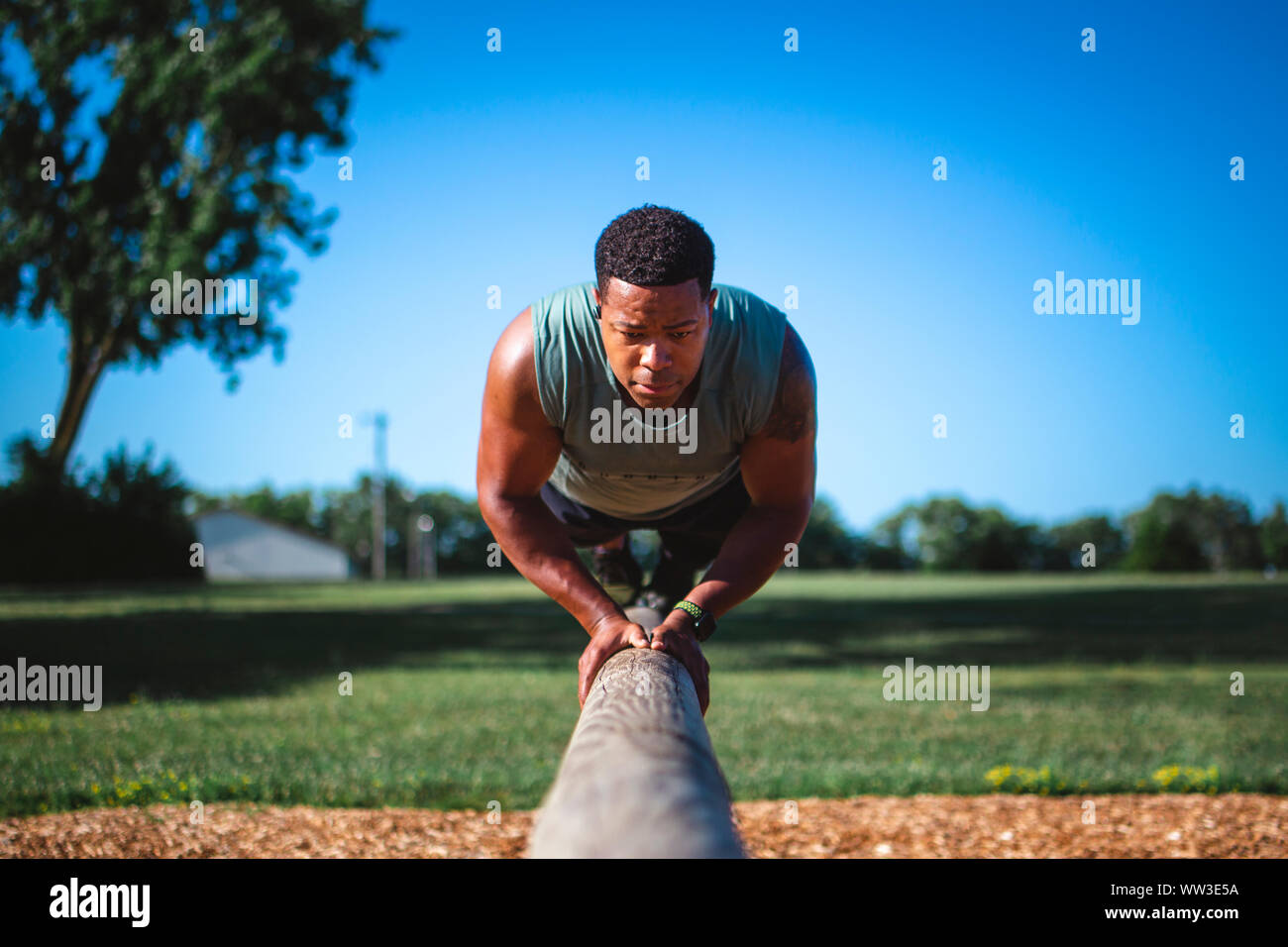 A strong athlete balances on single beam in park performing pushups Stock Photo