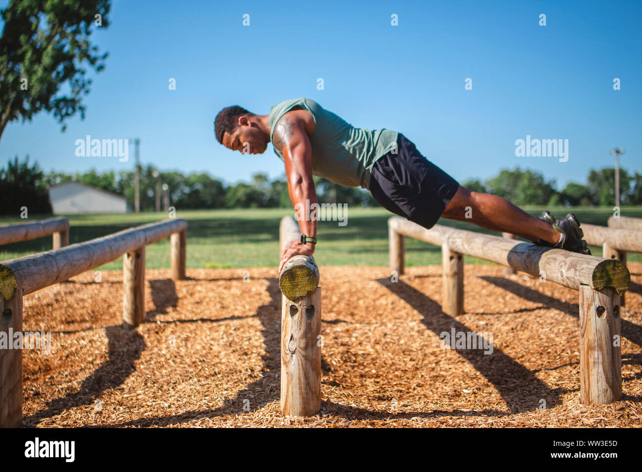 A strong man performs pushups stretched across wood beams in park Stock Photo