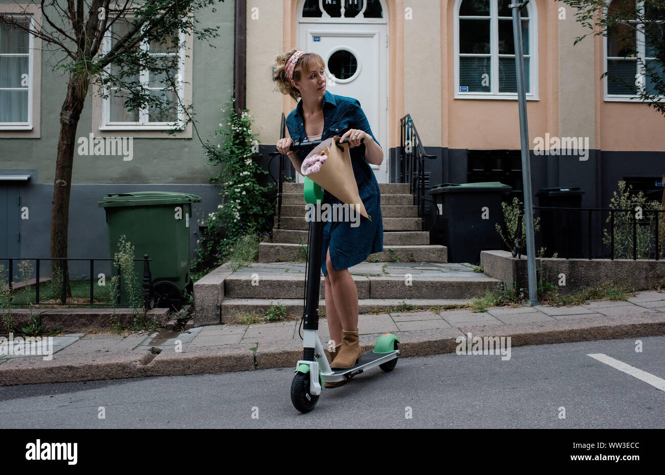 woman travelling on a city rental scooter holding flowers Stock Photo
