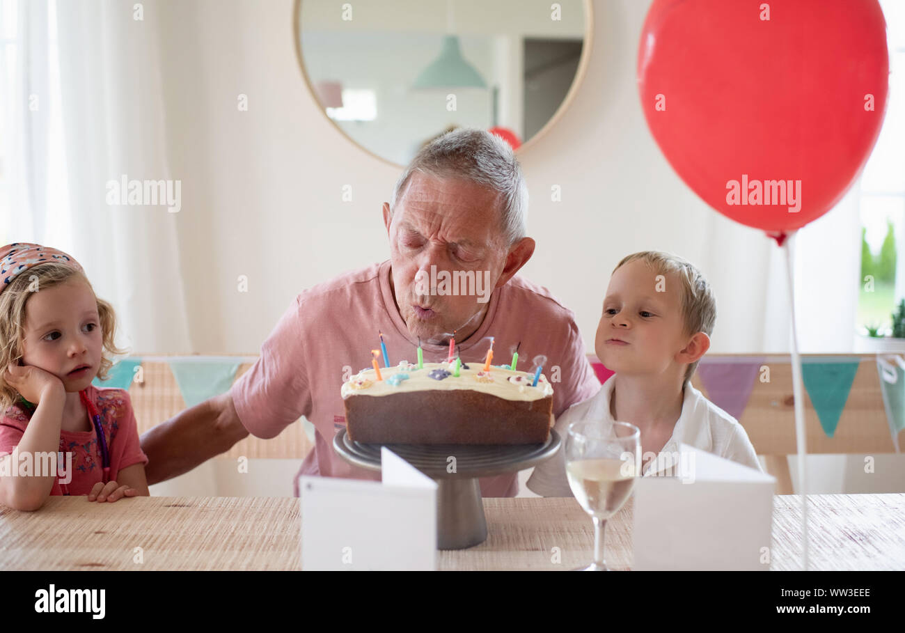 grandad sat with his grandchildren on his birthday blowing candles Stock Photo