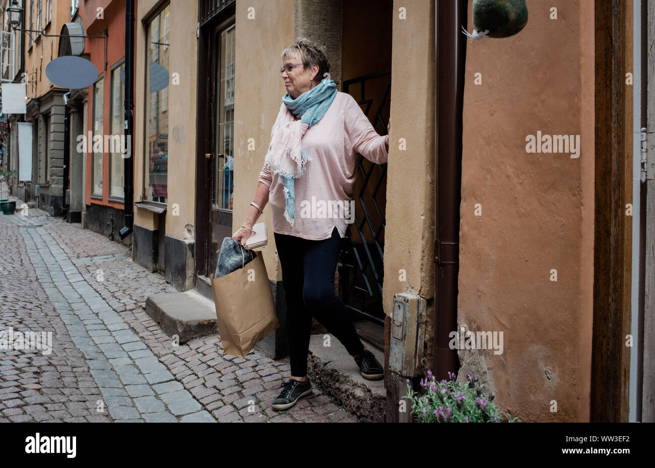 older woman walking out of a cobbled street shop in Europe travelling Stock Photo