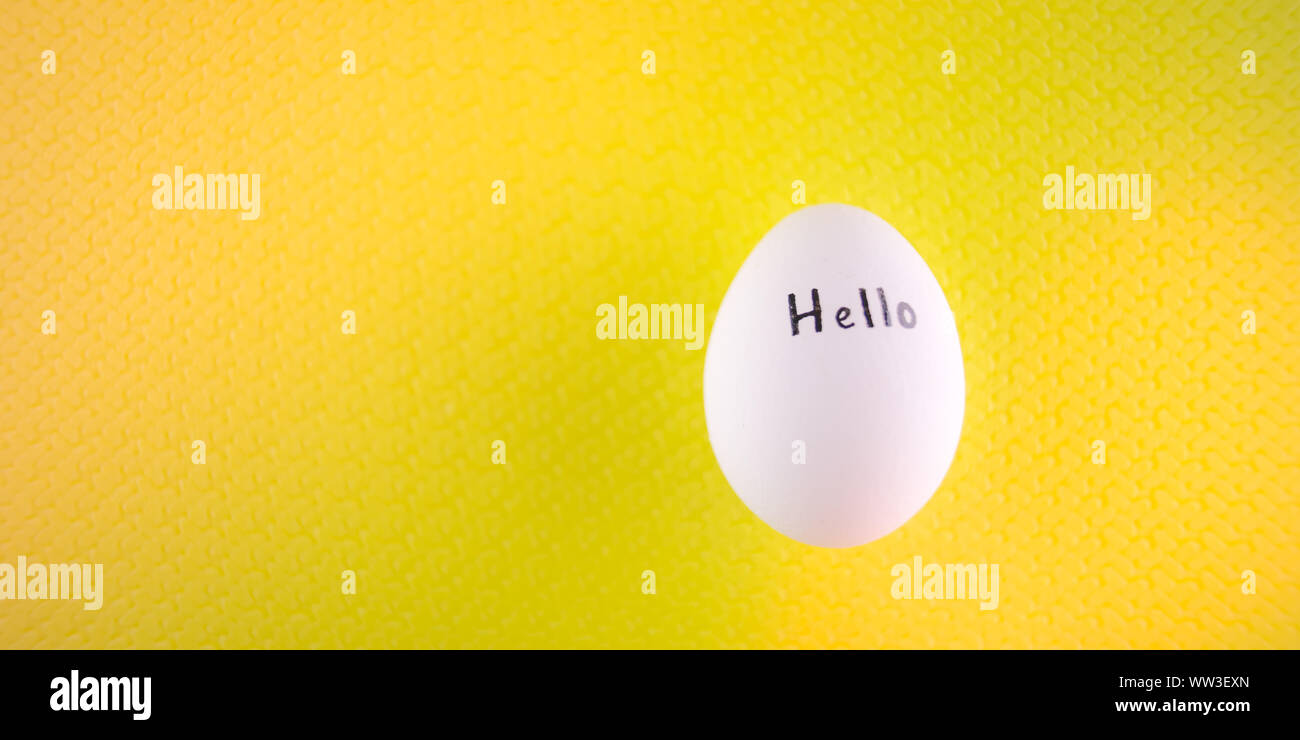 White chicken egg with black inscription hello on a yellow background. Stock Photo