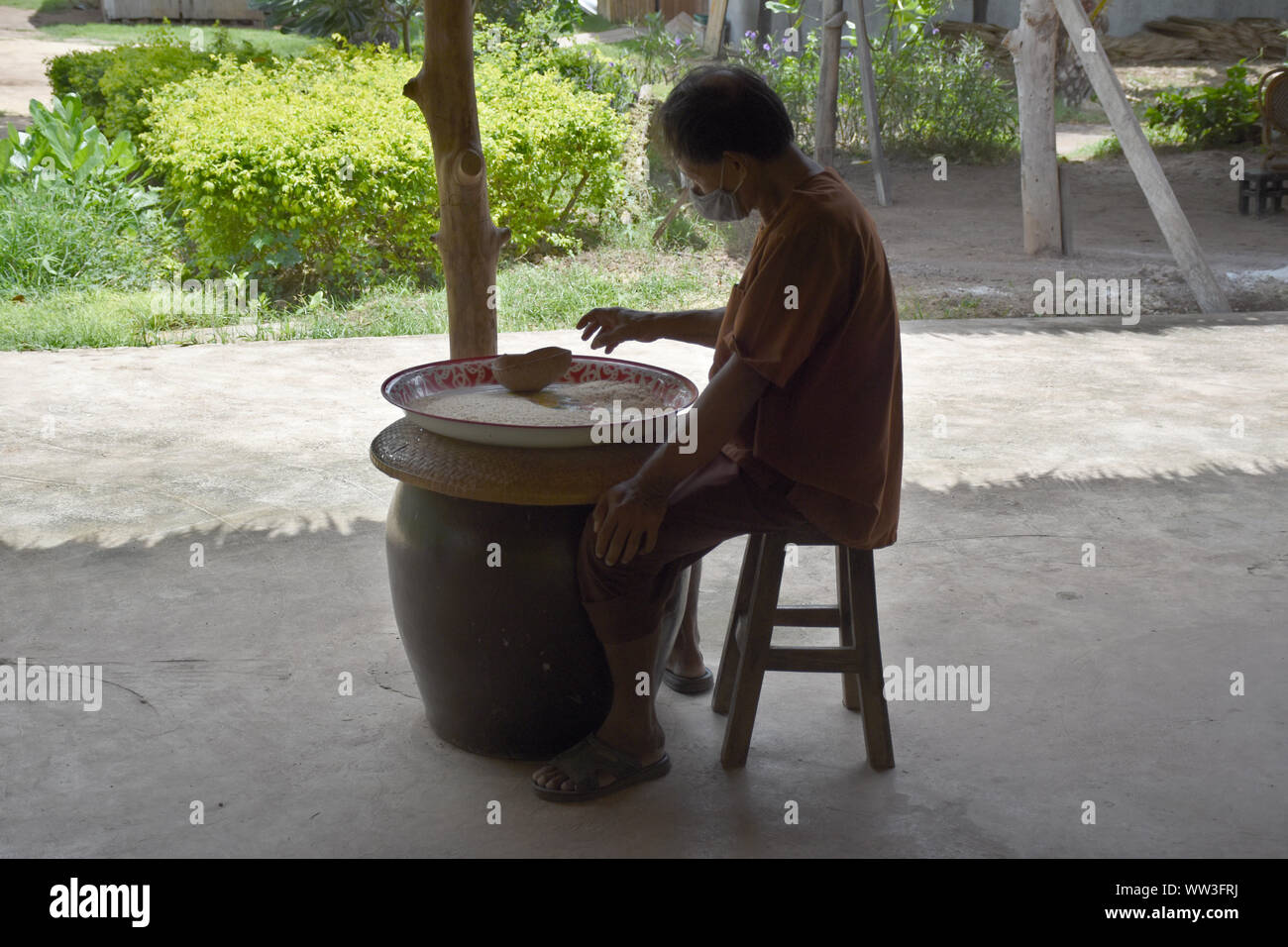 Kanchanaburi, Thailand, 09.09.2019: A local Thai man in traditional Thai, Siamese dress is sorting rice, separating the bad ones from the good ones in Stock Photo
