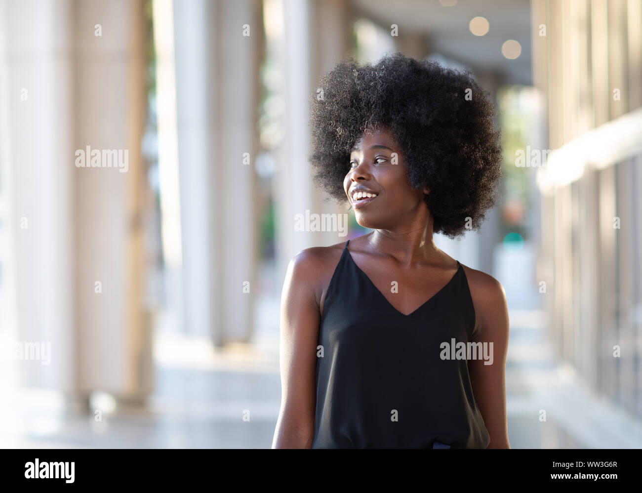 Smiling young black woman walking in the city looking to the side ...