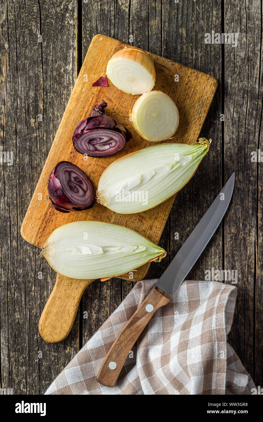 Halved fresh bulbs. Cut onions and knife on old wooden table. Top view. Stock Photo