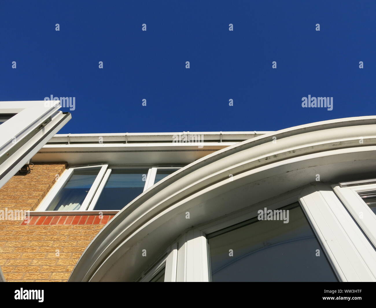 Abstract photo of verticals, horizontals and curves in white pvc on a modern house elevation looking up towards a very blue sky Stock Photo