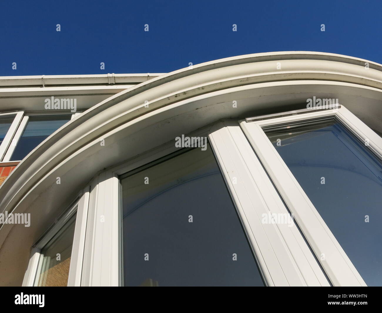 Modern house architecture with an abstract photo looking up at a curved bay window and straight roofline in white pvc, against a brilliant blue sky. Stock Photo