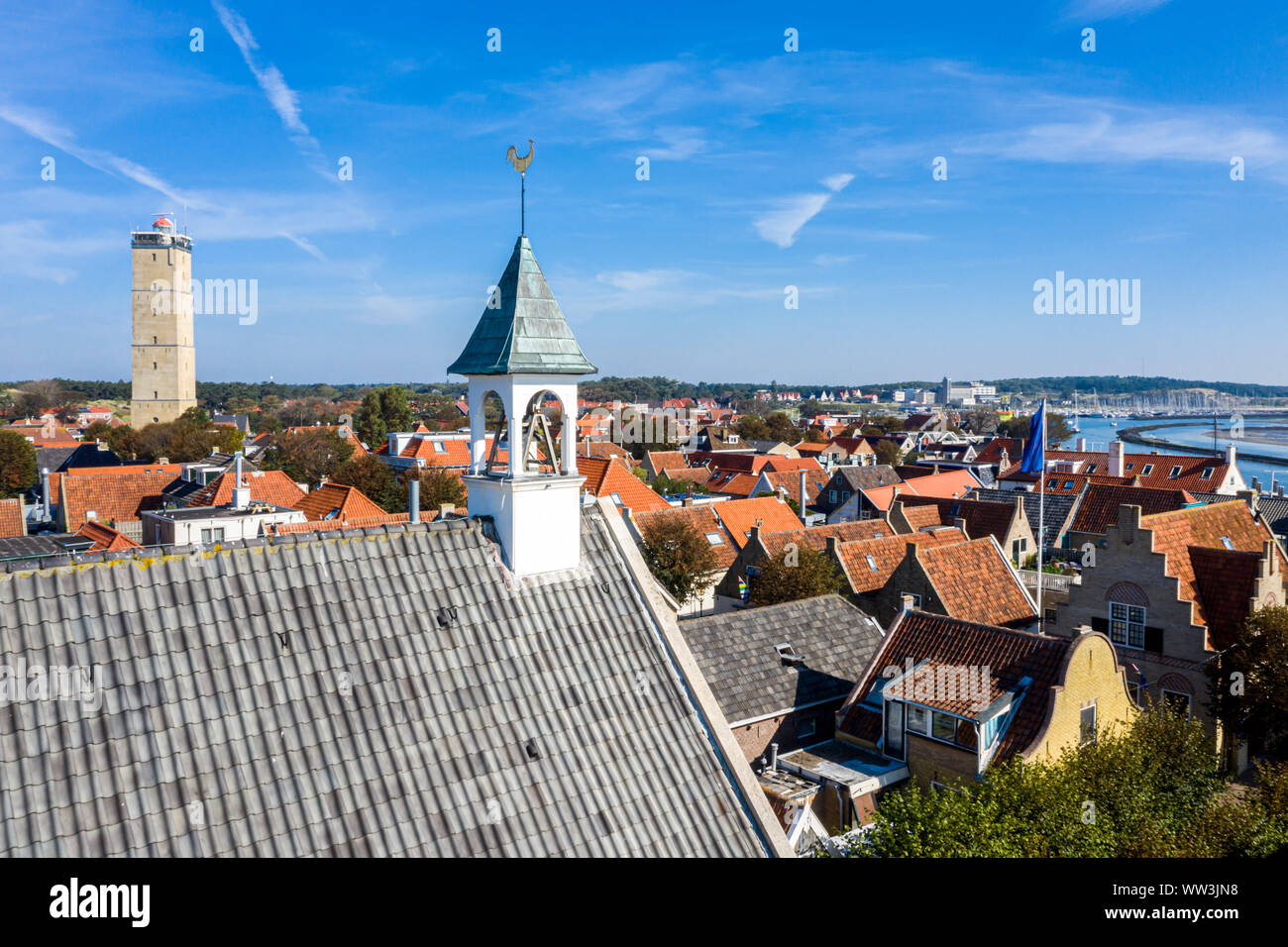 Aerial close up of Westerkerk church bell tower with rooster weather vane in West-Terschelling town, Netherlands. Brandaris lighthouse, harbour and hi Stock Photo