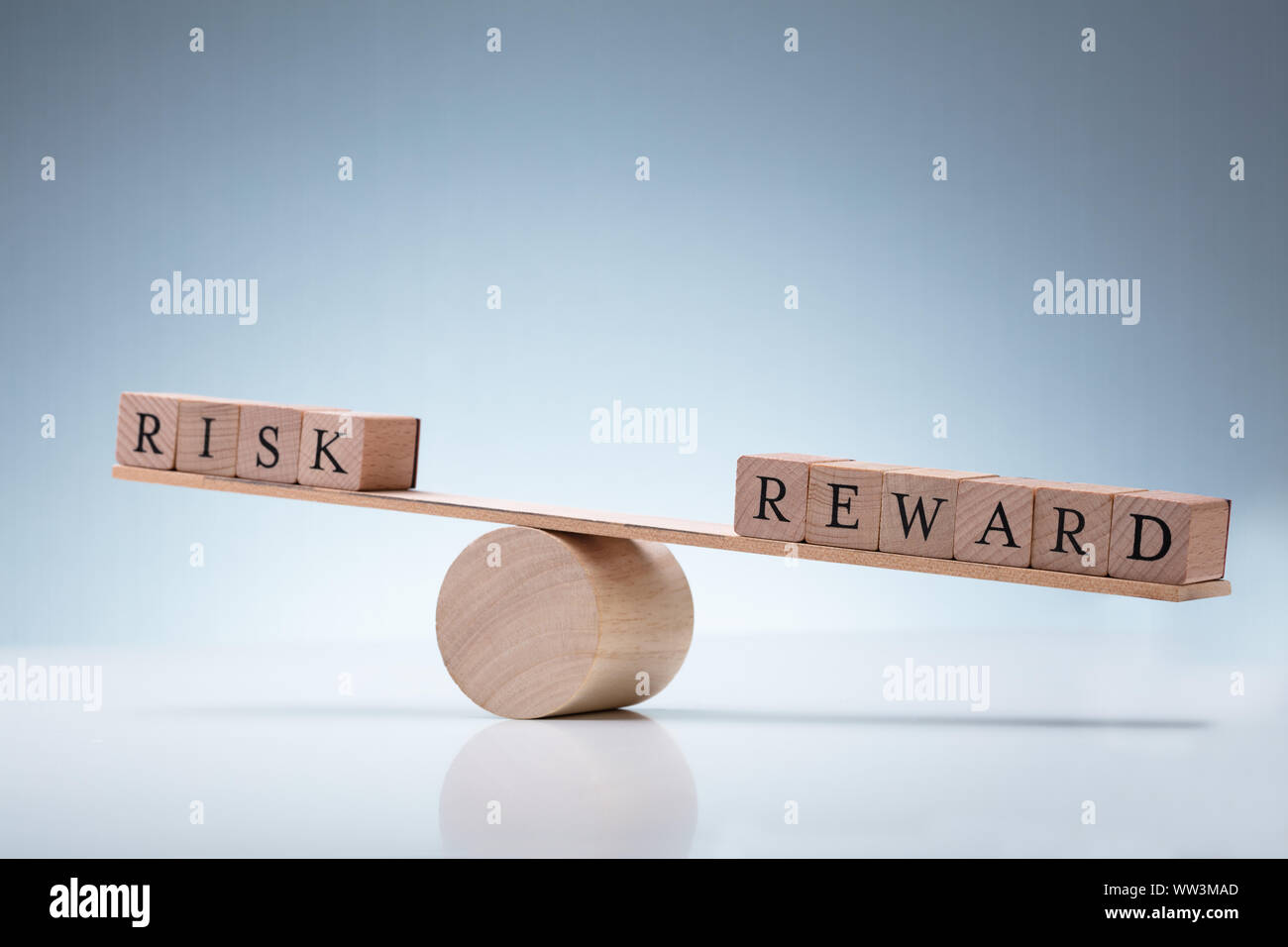 Close-up Of A Wooden Seesaw Showing Imbalance Between Risk And Reward On Reflective Background Stock Photo