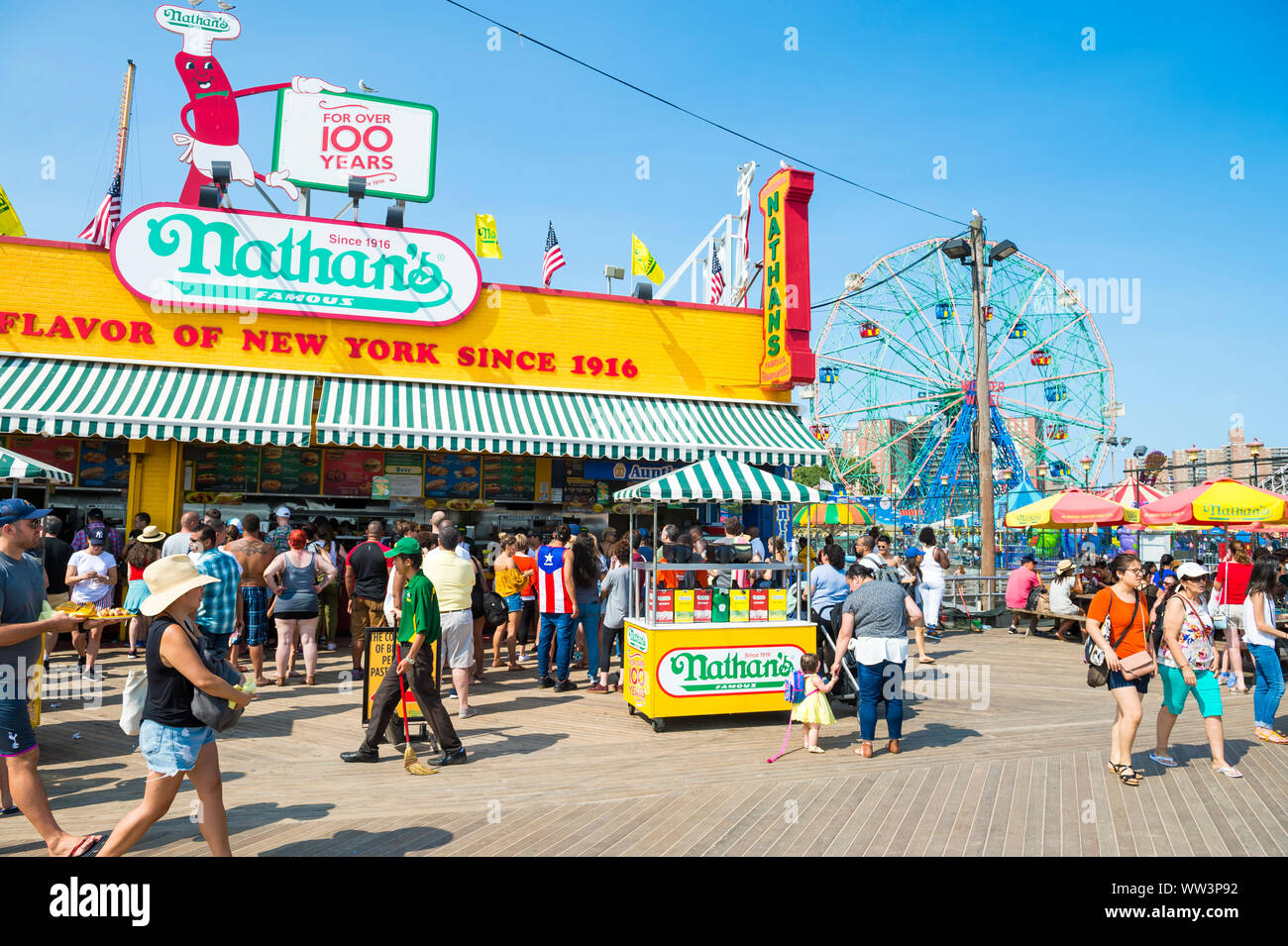 NEW YORK CITY - AUGUST 20, 2017: Visitors walk the iconic wooden Coney Island boardwalk outside the famous Nathan's hot dog stand on a hot summer day. Stock Photo