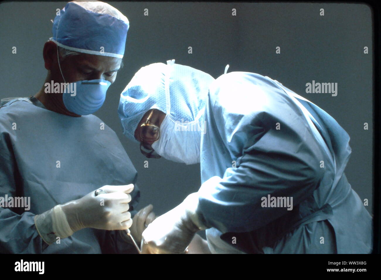 Surgeons performing knee replacement in sterile surgical scene. Stock Photo