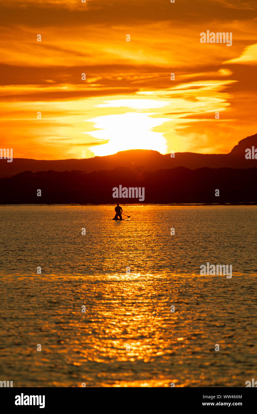 Paddle Boarder  silhouetted against the sunset over Anglesey, Taken from Rhosneigr beach. Stock Photo