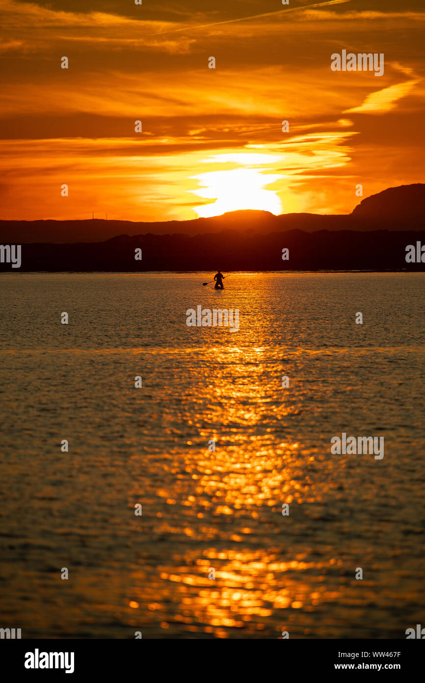 Paddle Boarder  silhouetted against the sunset over Anglesey, Taken from Rhosneigr beach. Stock Photo