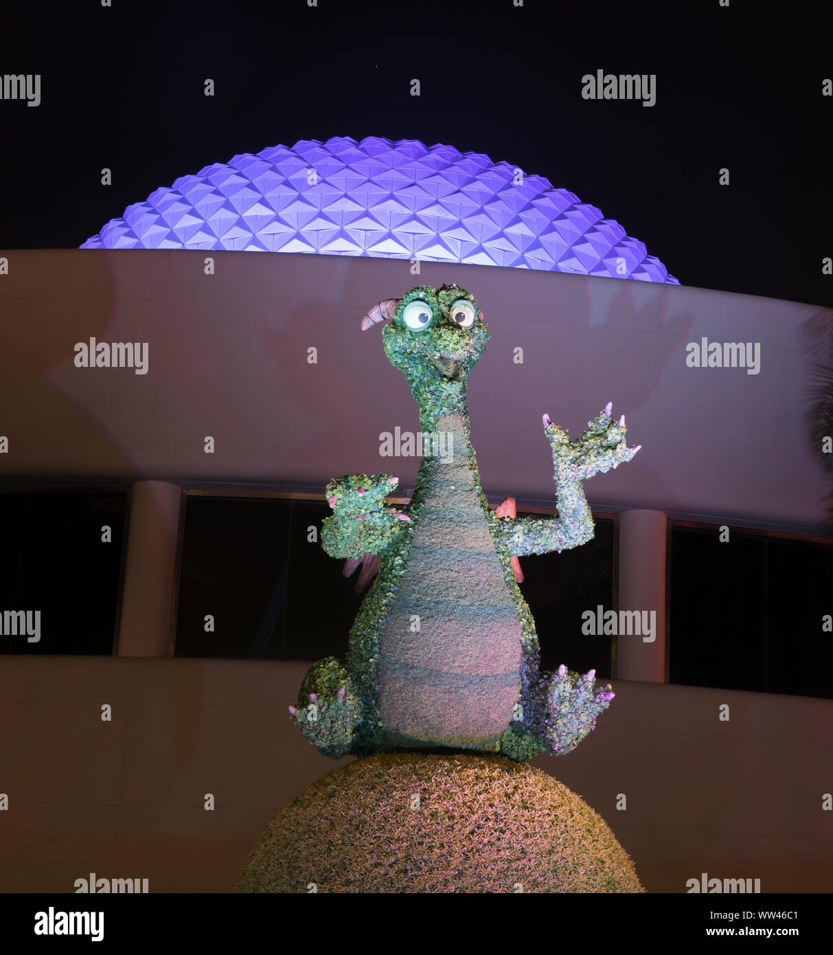 Epcot Center smiling and lighted Imagination Dragon at night, with the Epcot Spaceship Earth sphere in background. lit in purple. Stock Photo