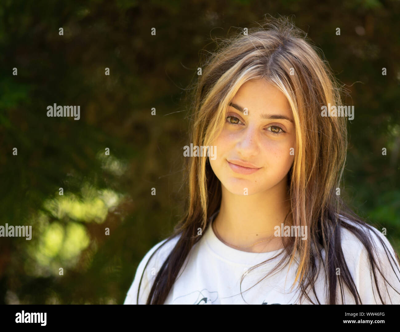 Beautiful natural close up portrait of a young woman on a blurred green forest background with highlights in her hair having an attitude. Stock Photo