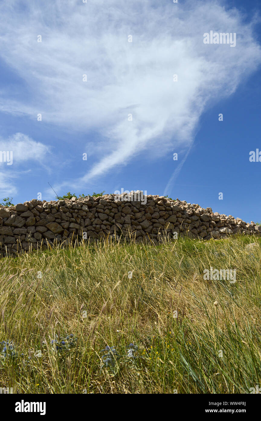 Handmade stone wall on top of hill, blue sky background Stock Photo