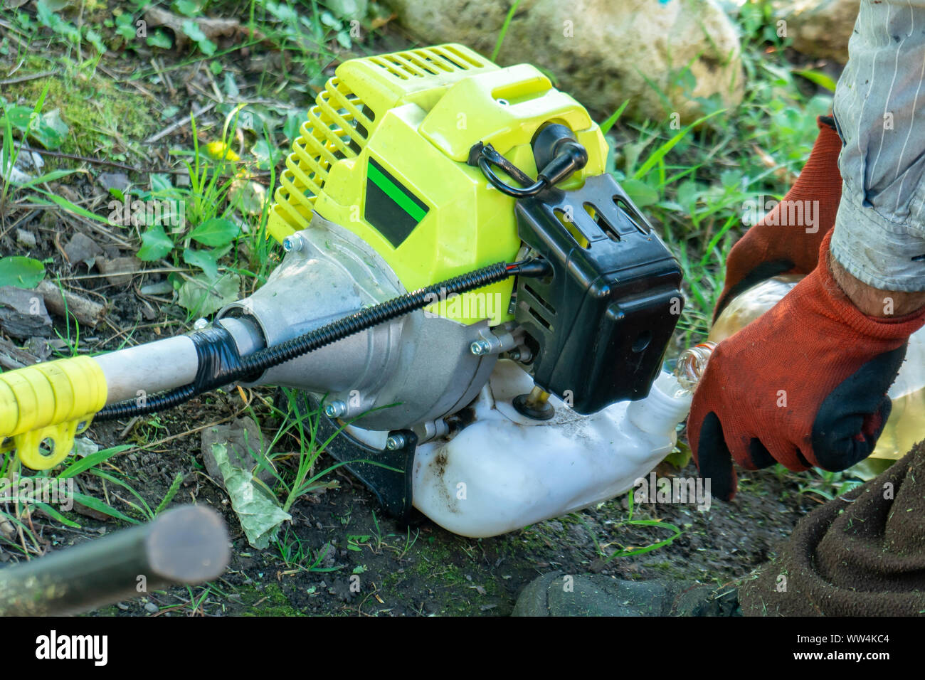 Farmer adding petrol gas to the gasoline tank of the trimmer brushcutter in the field. Technology. Stock Photo