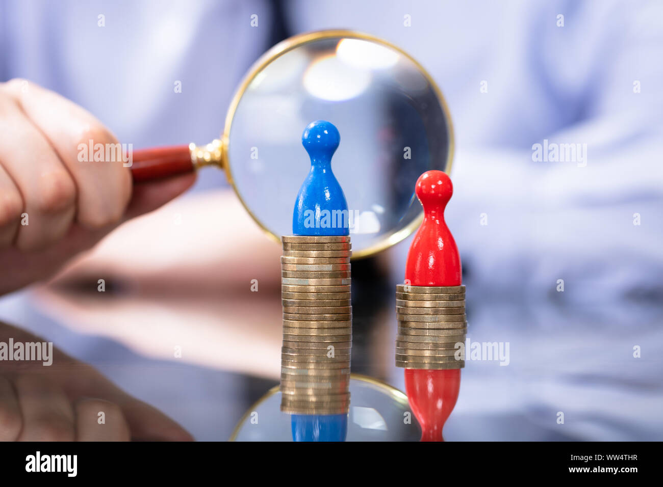 Man Looking With Magnifying Glass At Two Coin Stacks. Gender Pay Gap Stock Photo