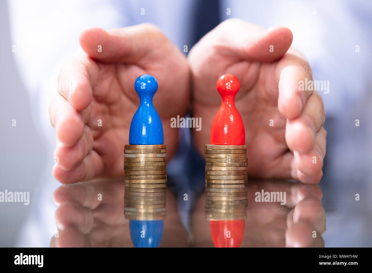 Man Protecting To Coin Stacks. Equal Pay For Men And Women Stock Photo