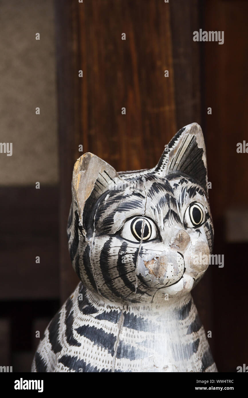 Gotoku ji Temple, Tokyo, Japan.  The carved wood figure of actual  likeness of Maneki Neko, also known as a Lucky Cat sits by the temple building. Stock Photo