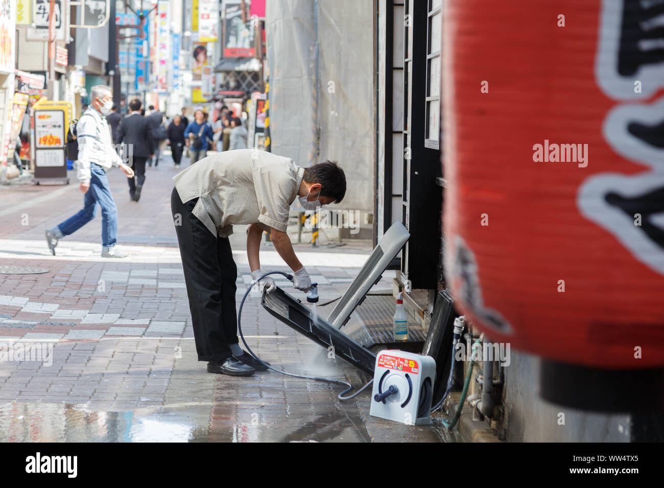 Shinjuku, Tokyo, Japan.  A young male restaurant worker in uniform cleans air conditioner parts outside on the street before the shop opens. Stock Photo
