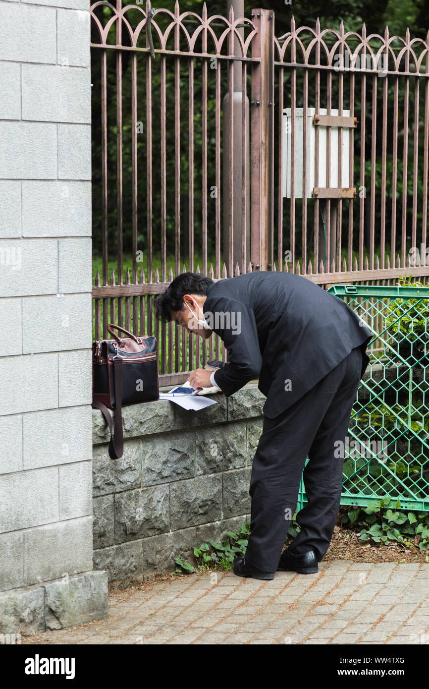 A Japanese businessman works outside park fence with a physically uncomfortable manner during work hours in Tokyo, Japan. Stock Photo