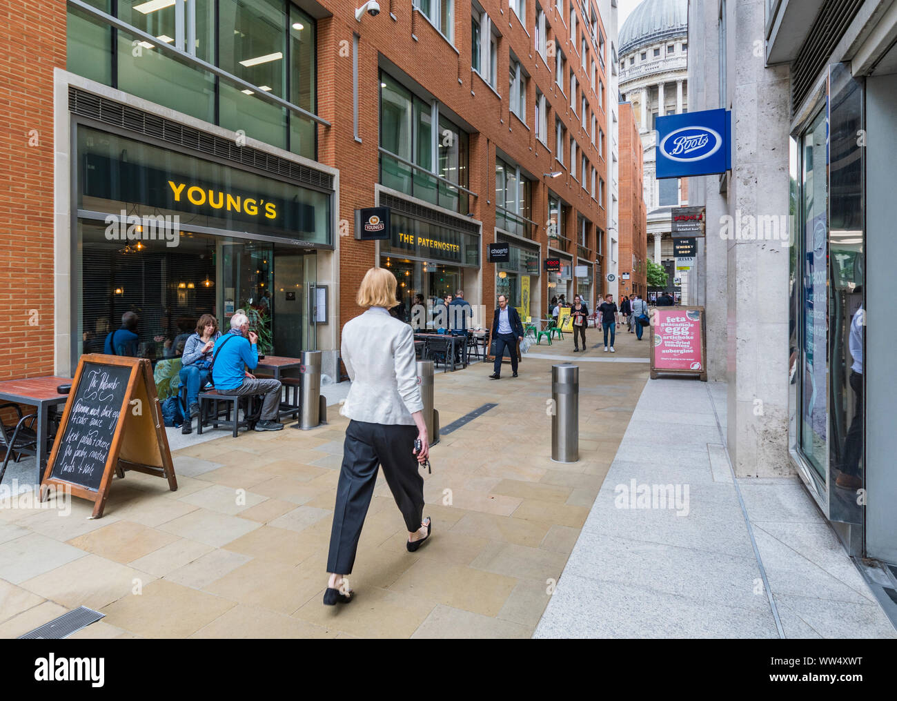 People walking along by shops in a pedestrian passageway in Queens Head Passage, Paternoster Row, London, England, UK. Stock Photo