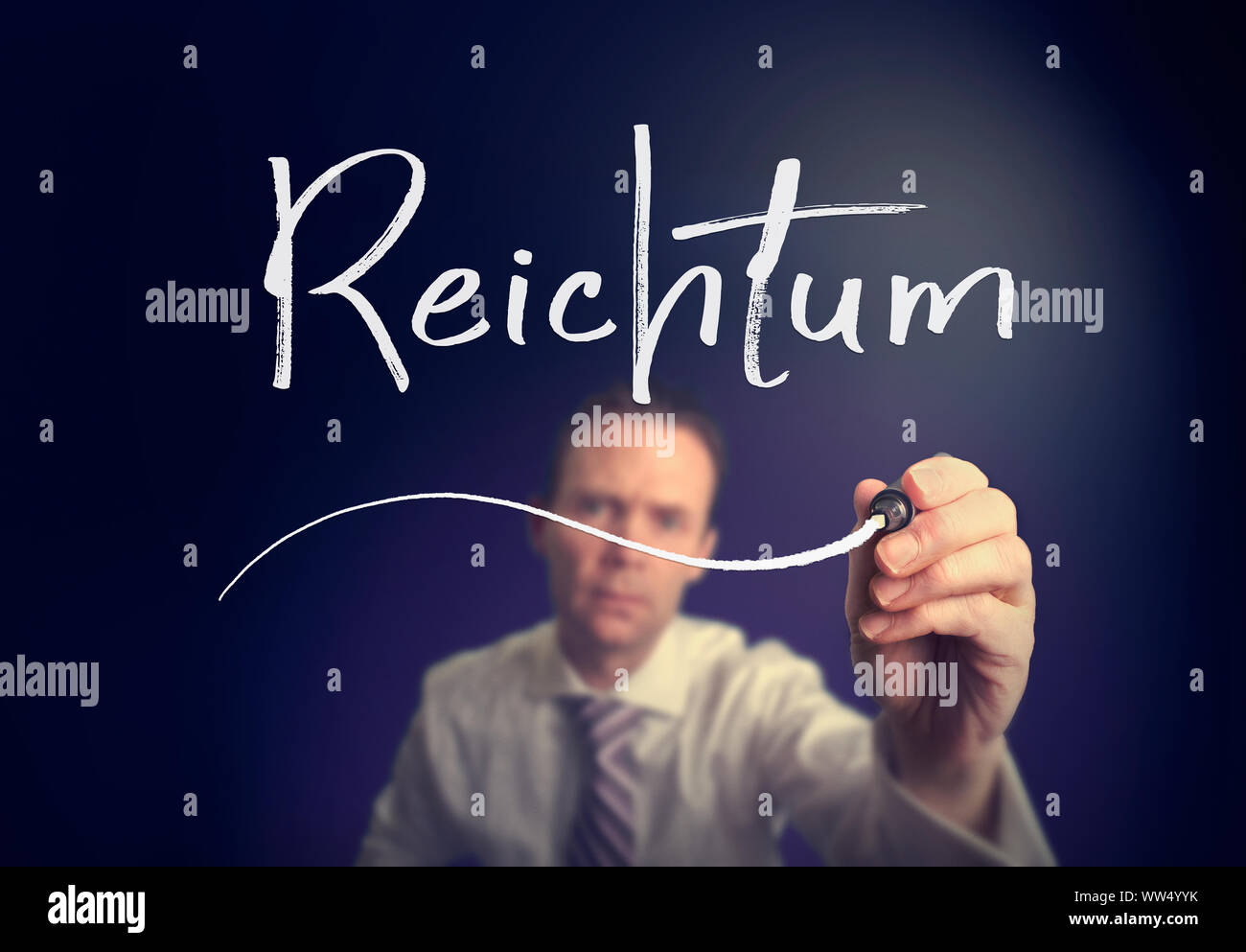 A businessman writing a Wealth "Reichtum" concept in German with a white pen on a clear screen. Stock Photo