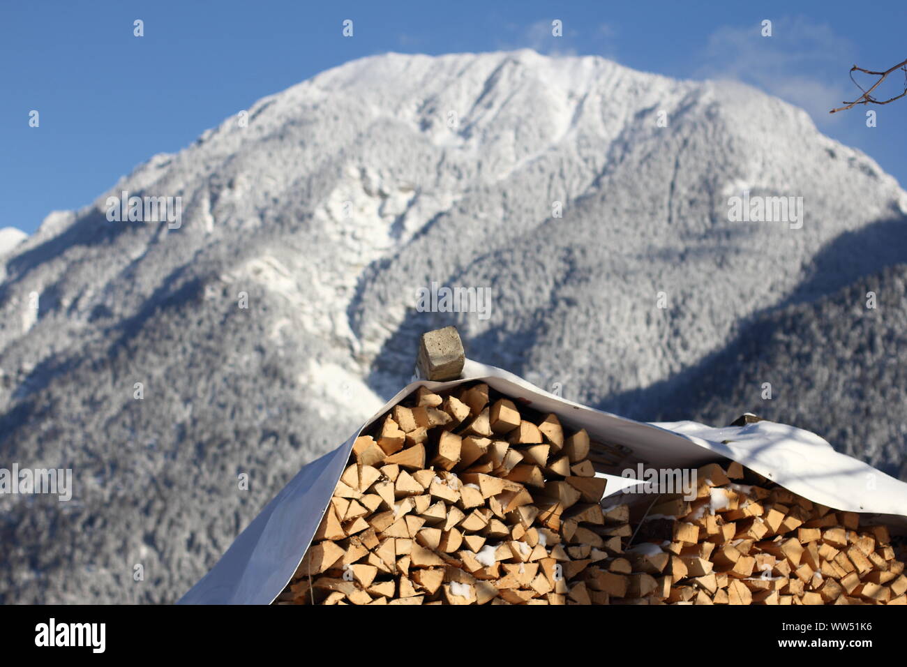 Stacked wood in front of a snowcapped mountain and blue sky in Upper Bavaria, Stock Photo