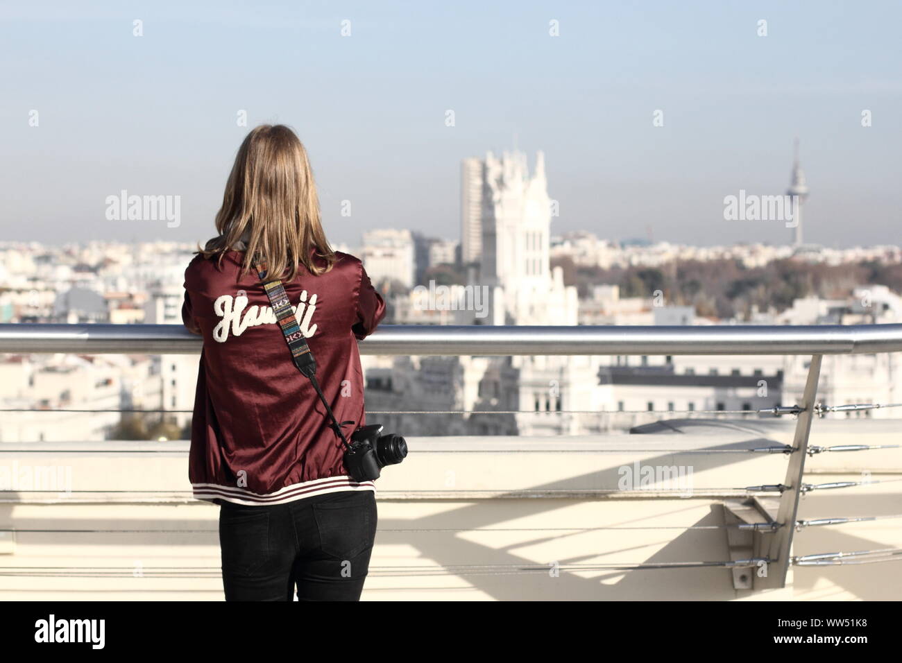 A young woman standing at the railing of a roof terrace and looking over Madrid, Stock Photo