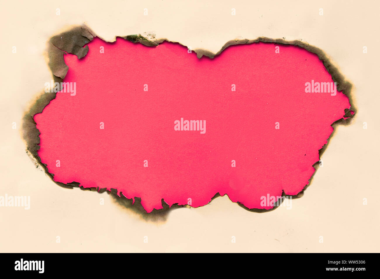 Burnt hole in yellow paper with burned edges, flat lay on crimson red paper with copy-space Stock Photo