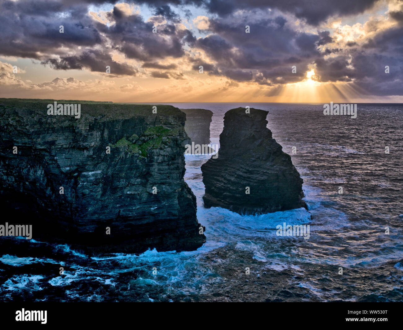 Ireland, County Clare, rocky coast at the Loop peninsula, rock towers in the surf, light of the evening sun Stock Photo
