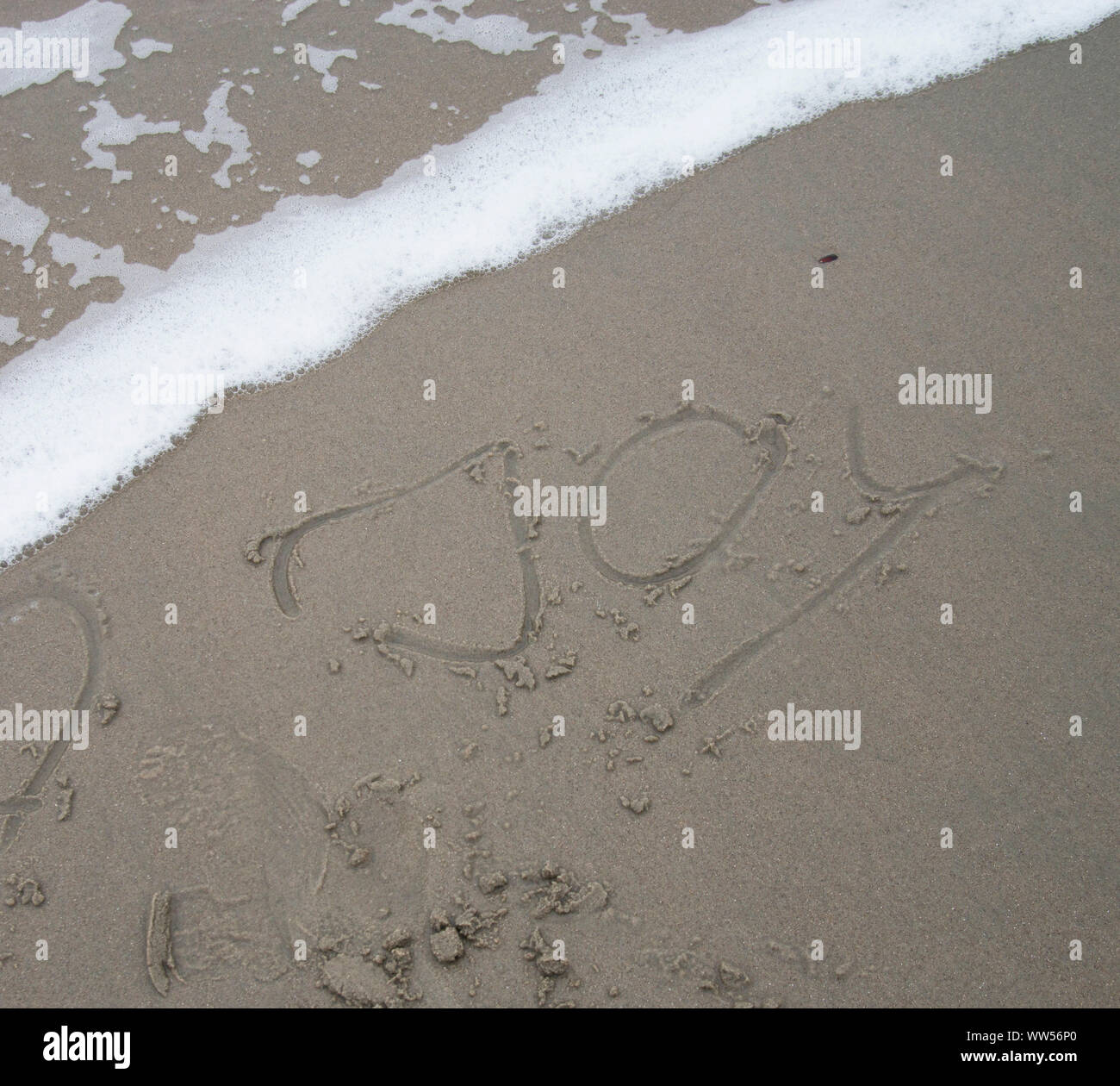 Word Joy in sand in front of small wave Stock Photo