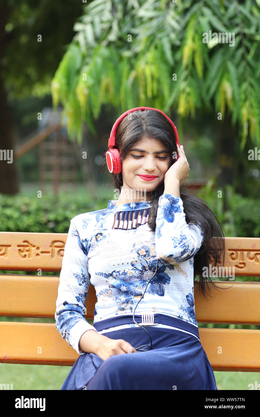 Relaxed teenage girl sitting of park bench and listening music by using headphone Stock Photo