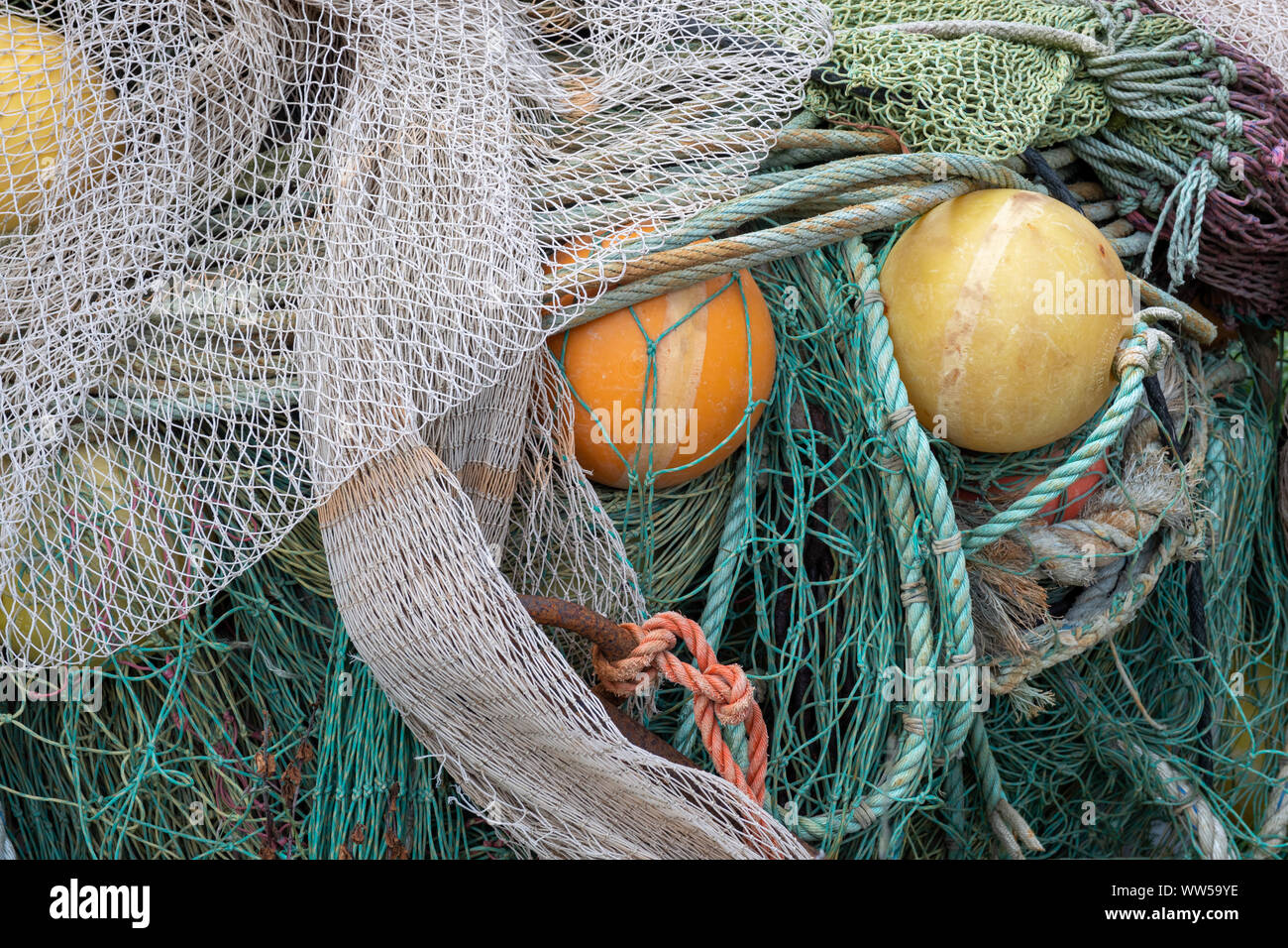 Old green and grey fishernet and other fishermens equipment, yellow and orange lifting bowls Stock Photo