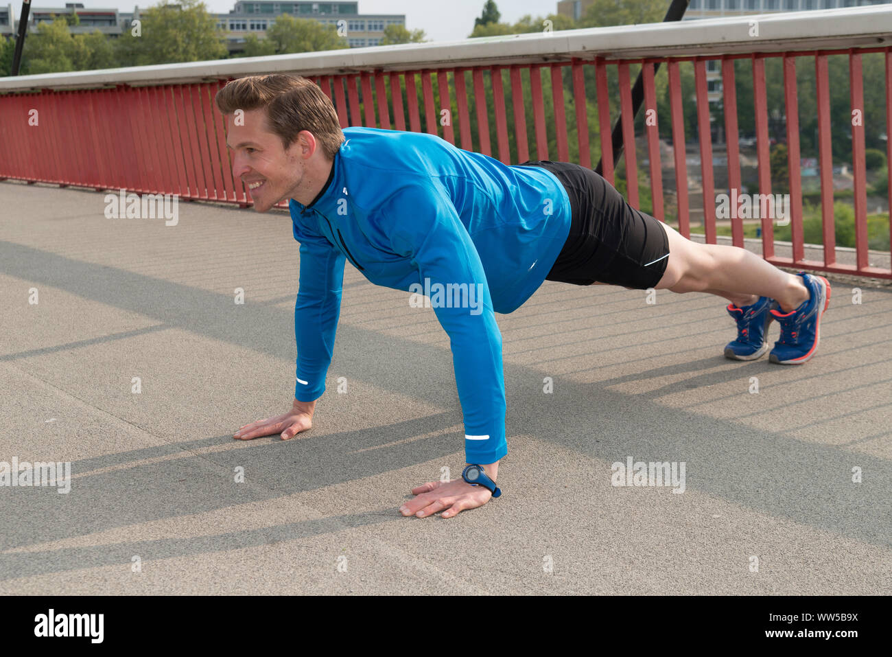 Man in blue tracksuit top doing push-ups on a bridge Stock Photo