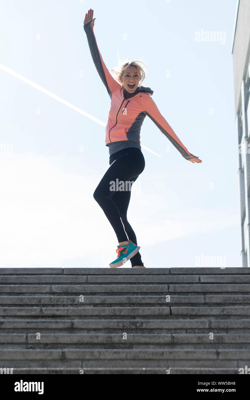 Woman in sports clothes standing cheering on top of stairs outside Stock Photo