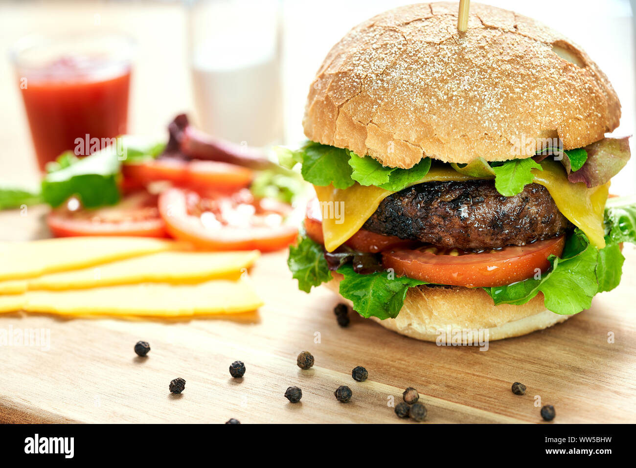 A cheese burger in a crusty bun with lettuce and tomatoes on a chopping