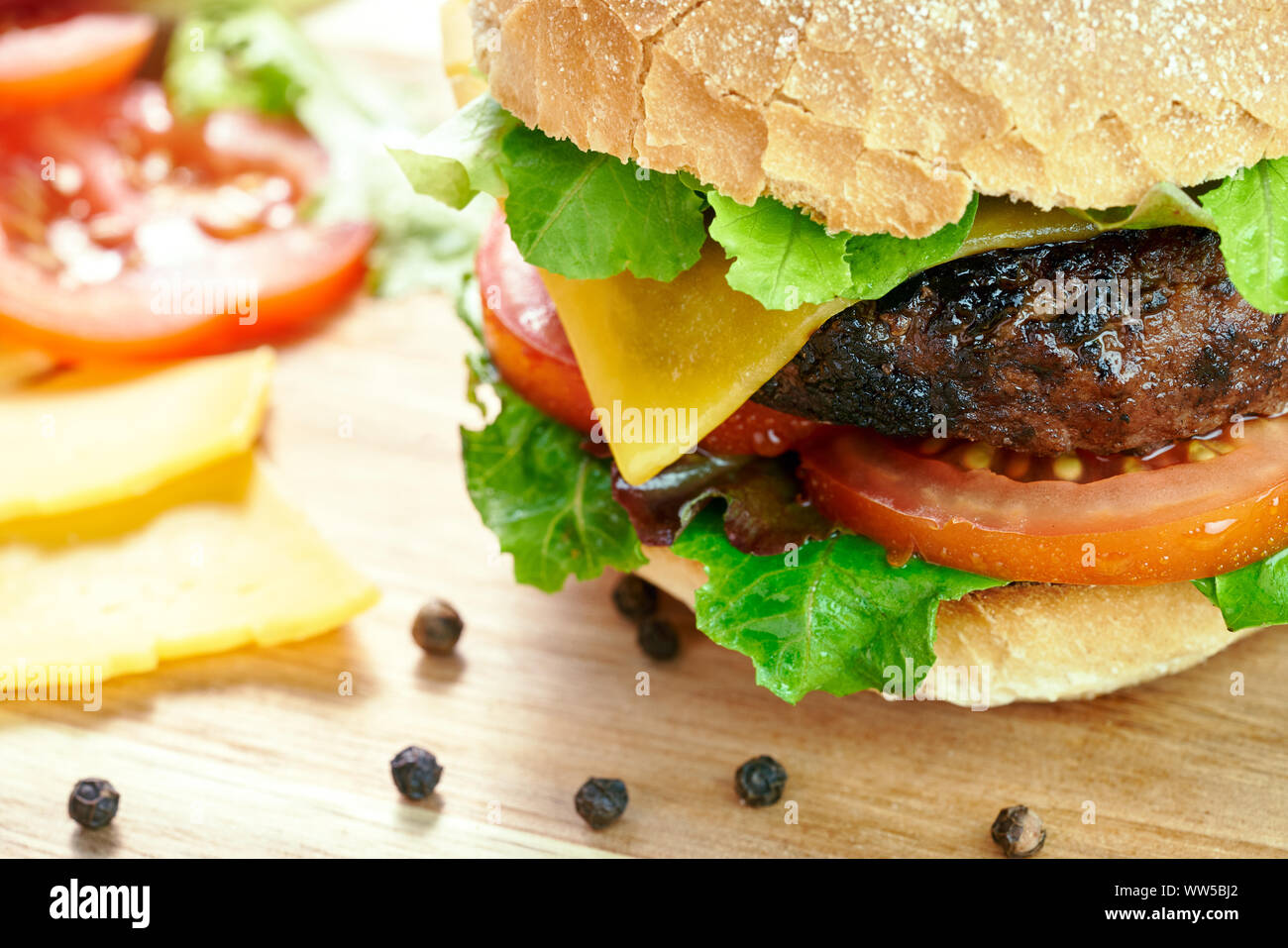 A cheese burger in a crusty bun with lettuce and tomatoes on a chopping