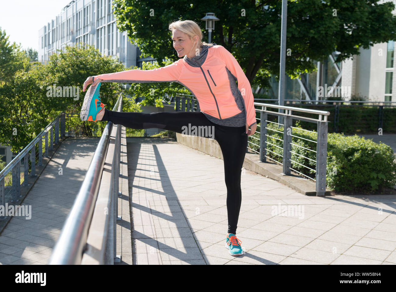 Woman in sports clothes at banister, stretching exercise, stretching leg, Stock Photo