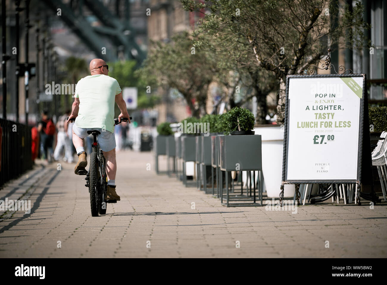 NEWCASTLE UPON TYNE, ENGLAND, UK - MAY 08, 2018: A cyclist riding past restaurants on the Newcastle Quayside Stock Photo