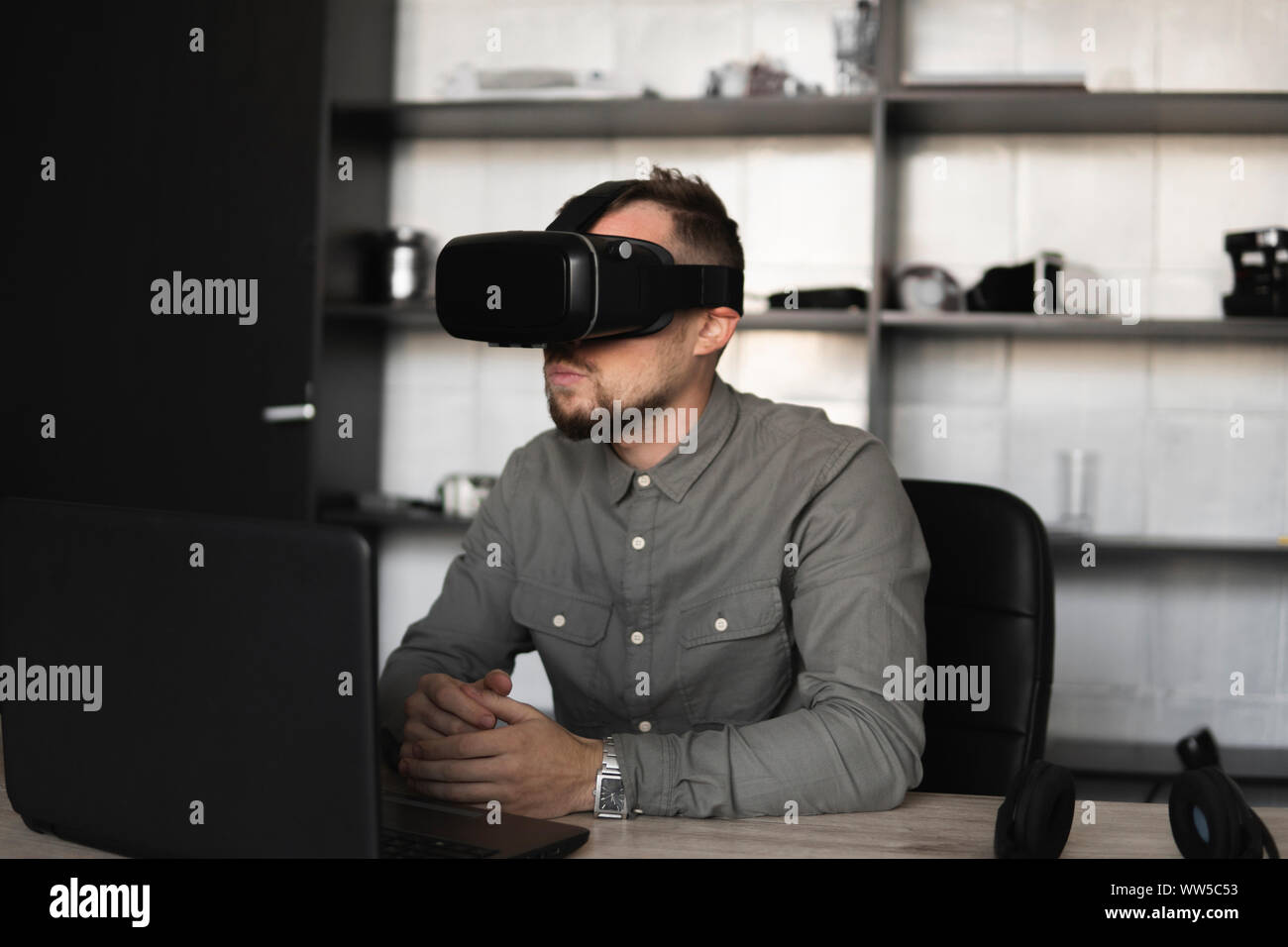 Young bearded man sitting against computer with virtual reality glasses ...