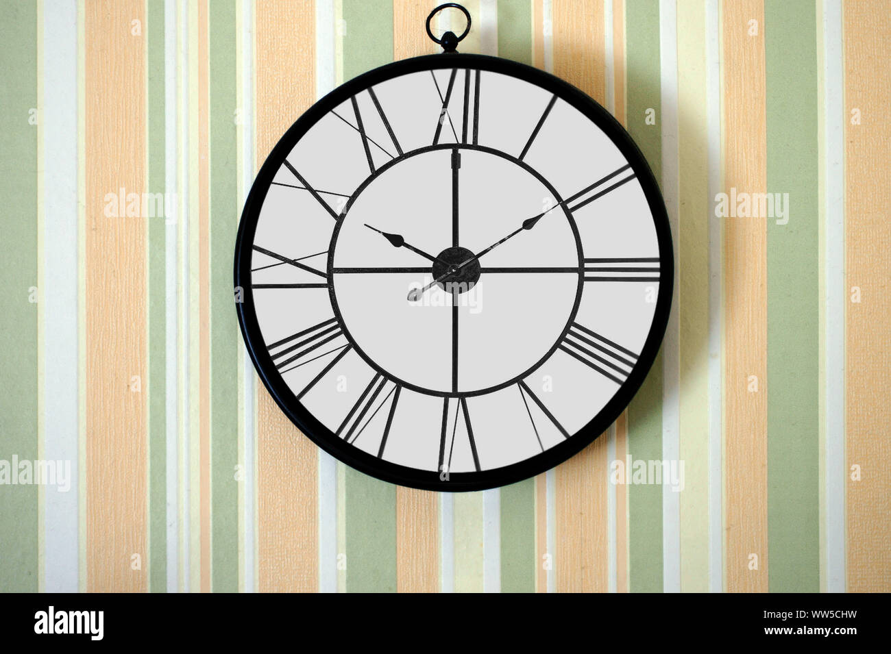 Close-up of a wall clock in front of a strikingly striped wallpaper, Stock Photo