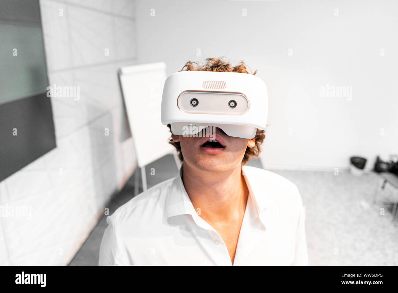 Amused and shocked Man wearing virtual reality goggles in modern contemporary bright co-working office. the VR experience. Stock Photo