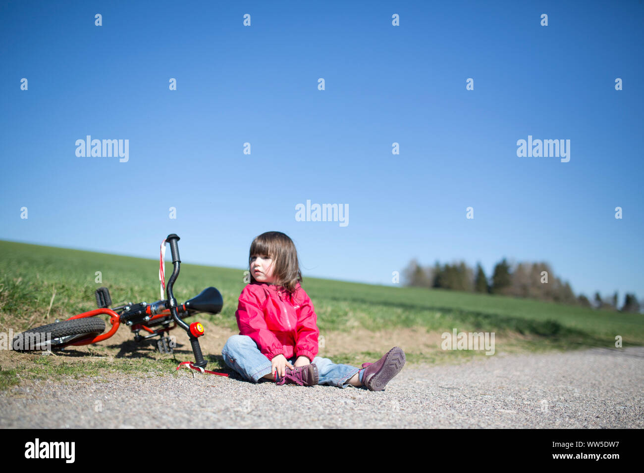 5 year old girl sitting beside red bicycle by the roadside hires stock