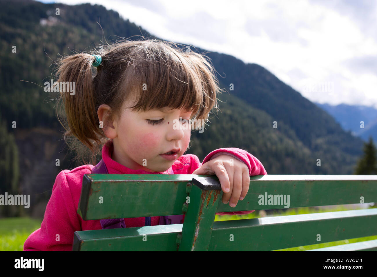 4-6 years old girl with plaits sitting on green bench Stock Photo