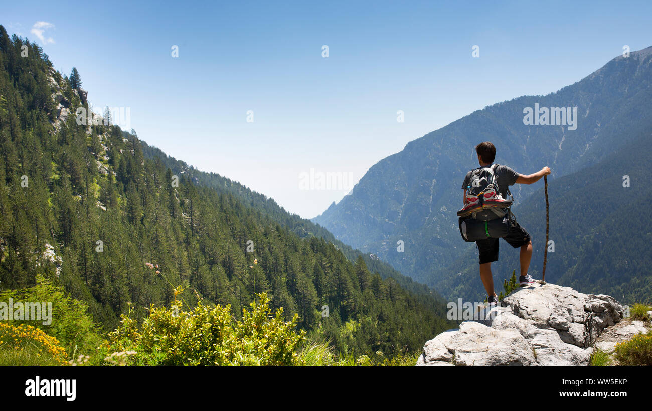 30-40 years old man with backpack standing on rock ledge looking in the valley Stock Photo